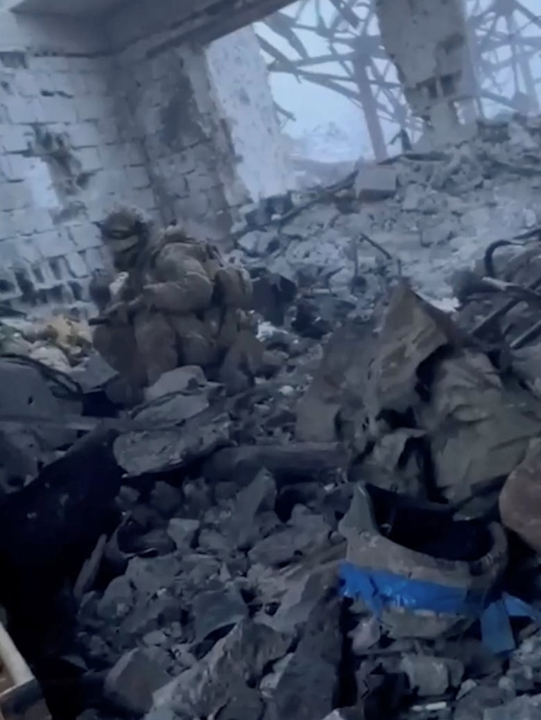 A soldier sits in the rubble of a nearly destroyed building.
